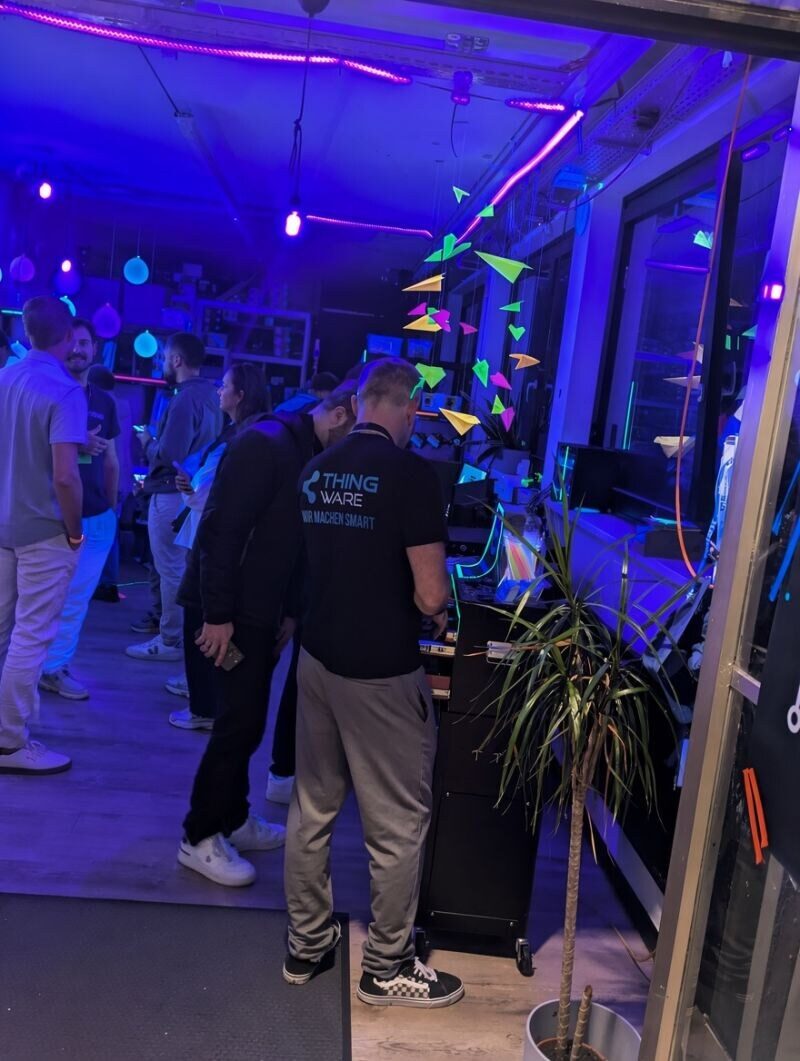 Foto: Gäste an den Stationen in der Werkstatt, beleuchtet mit UV-Licht und Neonröhren